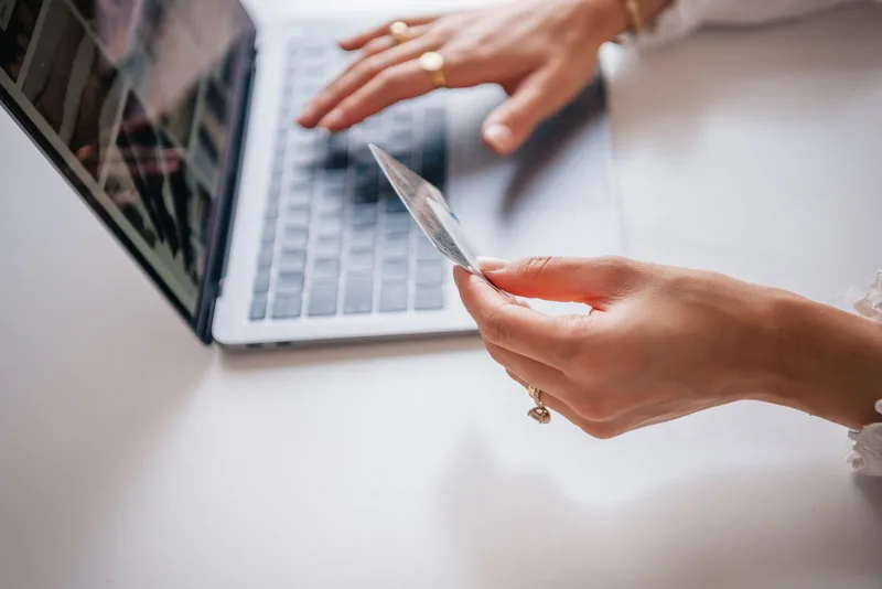 Tangan memegang kartu di dekat laptop saat transaksi belanja online