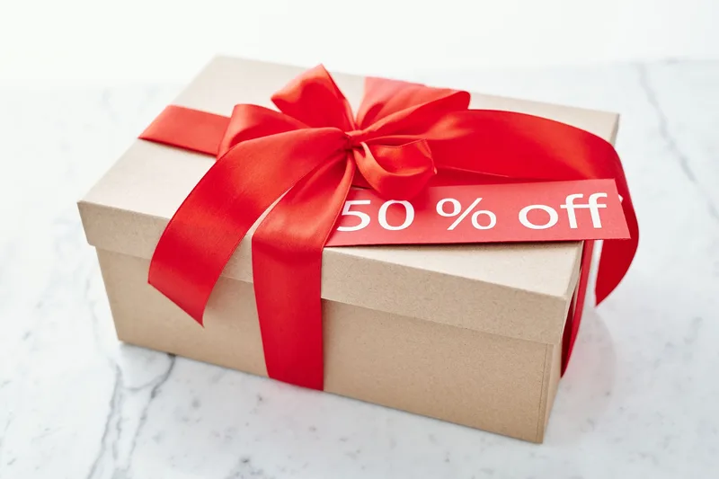 Kotak berpita merah dengan label diskon 50%, melambangkan promo voucher toko online