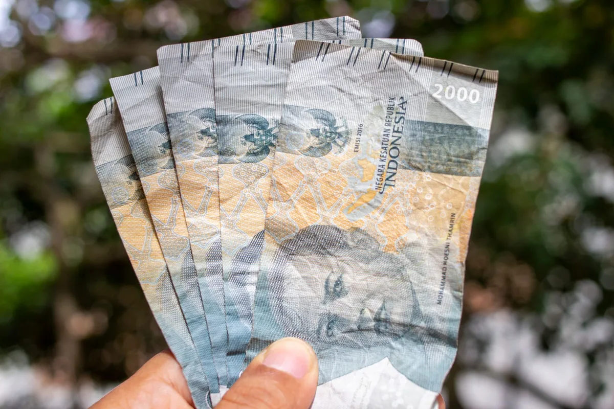 Tangan memegang beberapa lembar uang Rupiah, menggambarkan transaksi keuangan