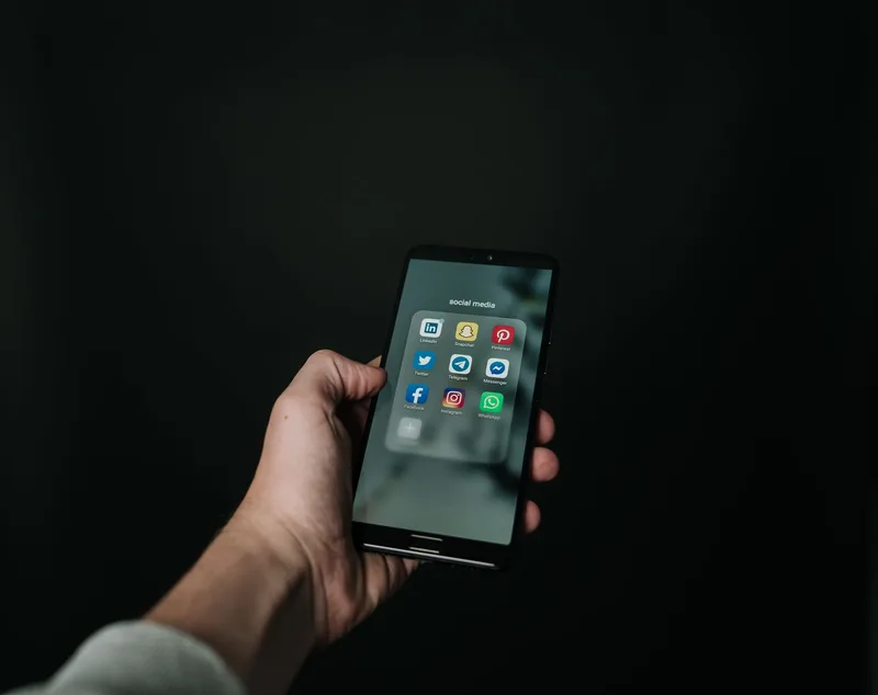 Tangan memegang smartphone yang menampilkan ikon-ikon aplikasi berbagi, ilustrasi tombol Bagikan di Shopee