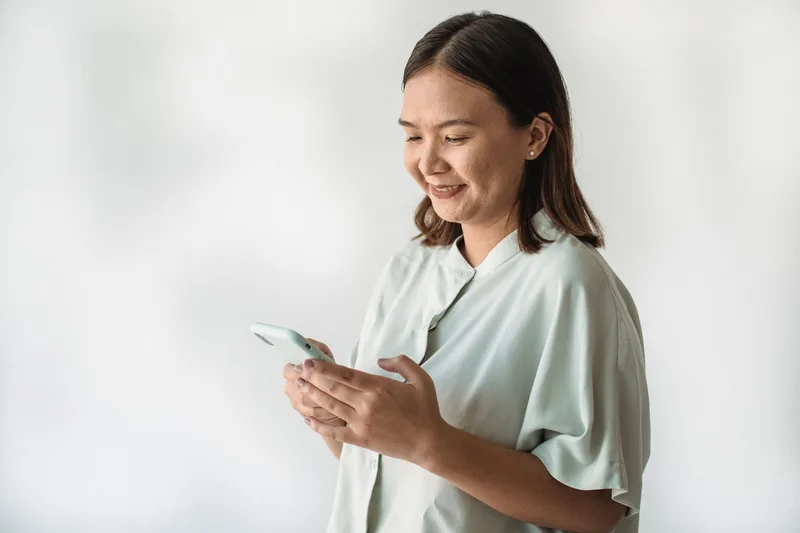 Wanita tersenyum memegang telefon pintar putih