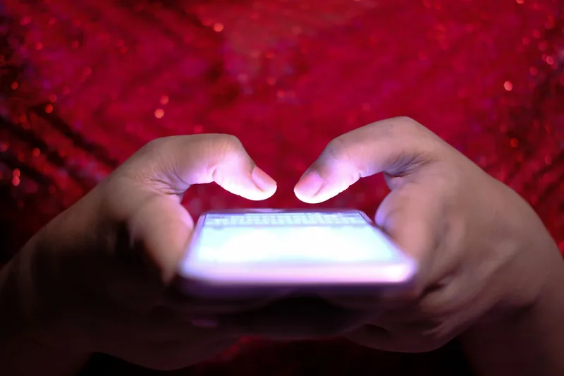 Tangan menaip di skrin telefon pintar yang bercahaya dalam pencahayaan malap