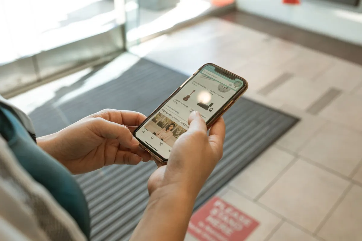 Two hands holding a smartphone that shows a shopping app with product listings