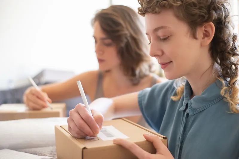 Two online sellers writing details on parcel boxes at a table