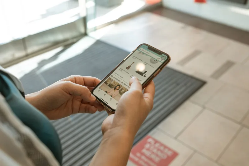 Tangan memegang smartphone membuka aplikasi marketplace untuk cek tren pencarian produk